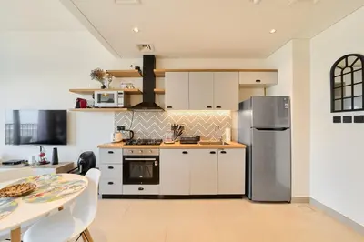 a kitchen with white cabinets and a stainless steel refrigerator at Chic 1BR With Balcony in Collective 2 Dubai Hills in Dubai