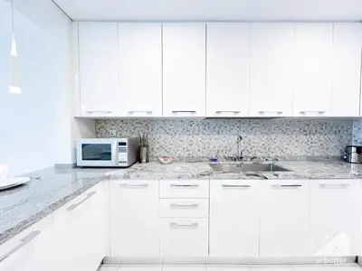 a white kitchen with white cabinets and a microwave at Stylish 1-Bedroom Retreat with Balcony Views in Dubai