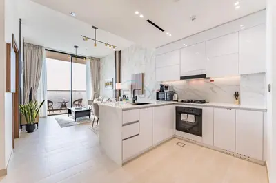 a kitchen with white cabinets and a living room at Sky Level 1BR with Lake View and City Glimpse, Close Proximity to Community Park, Binghatti Onyx, Jumeirah Village Circle by Deluxe Holiday Homes in Dubai