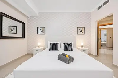 a white bedroom with a large white bed with two lamps at Elegant 2BR - Stunning Sea Views & Prime Location in Dubai