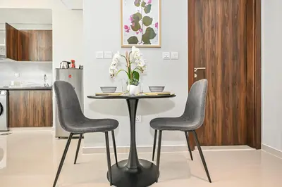 a table with two chairs and a table with flowers on it at Modern 1 Bedroom Apartment in Damac Hills 2 in Dubai