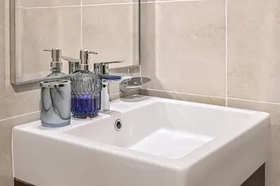 a white sink with two bottles and a mirror at Modern 1 Bedroom Apartment in Damac Hills 2 in Dubai