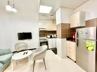 a small kitchen with a refrigerator and a table and chairs at Homes2Retreat - Modern Studio with Balcony in JVT in Dubai