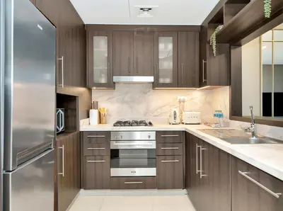 a kitchen with wooden cabinets and a stainless steel refrigerator at Kensington 1BR and Study with Sofa Bed Burj View Dubal mall link in Dubai