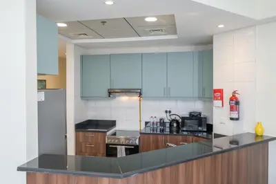 a kitchen with blue cabinets and a black counter top at Bright and Cozy 1BHK JVC by Czechin Great Location in Dubai