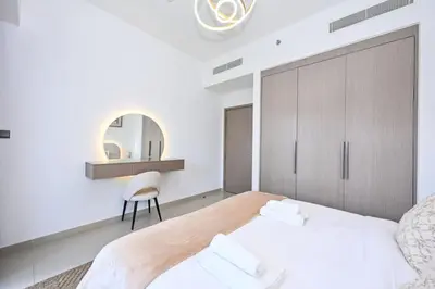 a white bedroom with a large bed and a chair at Modern 1BR in ACT Tower 1 in Dubai