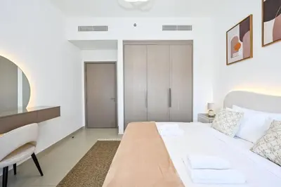 a white bedroom with a large bed and a chair at Modern 1BR in ACT Tower 1 in Dubai