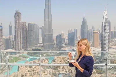 a woman holding a cup of coffee in front of a city at Full Burj Khalifa Panoramic View - Luxury Stay at Damac Maison Distinction in Dubai