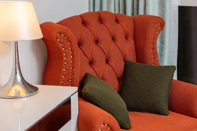 a red chair with two pillows on it next to a lamp at Full Burj Khalifa Panoramic View - Luxury Stay at Damac Maison Distinction in Dubai