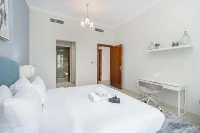 a white bedroom with a bed and a desk at Stylish 1BR DunyaTower Apartment 2min to DubaiMall in Dubai