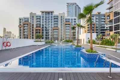 a swimming pool with palm trees and buildings at Modern Studio Near Downtown Dubai, Few Mins Walk to Hartland Greens Park, Azizi Riviera 43, Al Merkadh by Deluxe Holiday Homes in Dubai