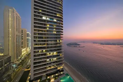 a tall building next to the ocean at sunset at Beachfront 2BR Grand Bleu Luxe Near Dubai Palm & Marina Hotspots in Dubai