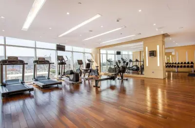 a gym with exercise equipment in a large room with wood floors at Modern JVC Studio with Pool Gym and Easy Access to Attractions in Dubai