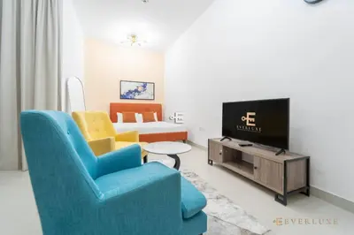 a living room with a blue chair and a tv at Perfect Midtown Studio Bright & Stylish in Dubai