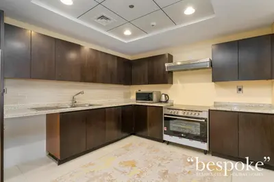 a kitchen with wooden cabinets and a sink at Bespoke Holiday Homes - Spacious 2BR Luxury Apartment with Stunning Palm Views, Balqis in Dubai