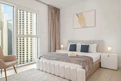 a white bedroom with a bed and a large window at Stylish 1BR Apartment in JBR with Beach Access & Dubai Marina Views in Dubai