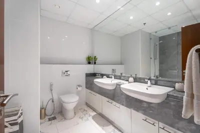 a white bathroom with two sinks and a toilet at 2BR Waterfront Apartment Nr Downtown in Dubai