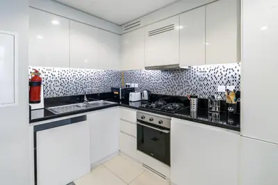a kitchen with white cabinets and black counter tops at Cozy 2BR Pool & City Views in Dubai