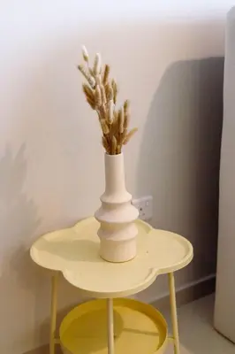 a white vase on a yellow table with a plant at Tropical Nest in Dubai