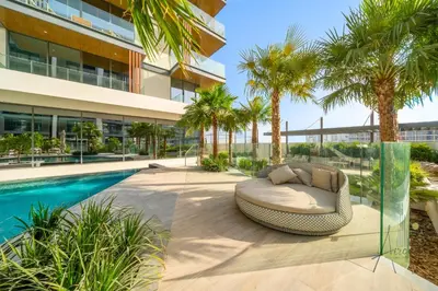 an outdoor patio with a couch and palm trees next to a swimming pool at Grove Luxurious Stu Best community Art & Design in Dubai