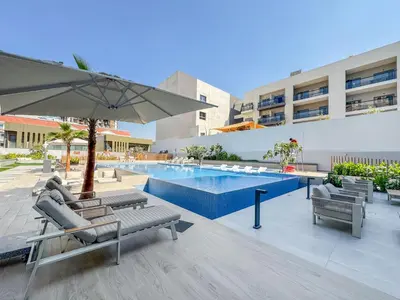 a pool with chairs and an umbrella next to a building at Luxurious Design Boutique Studio Hideaway JVC in Dubai