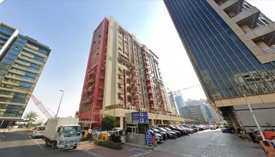 a tall red building with cars parked in a parking lot at Pleasing Partition Room Barsha Heights tecom in Dubai