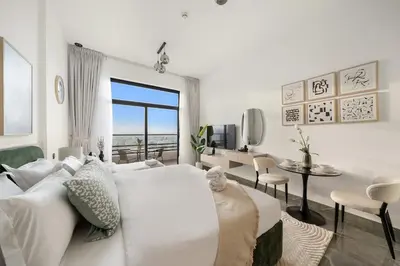 a white living room with a bed and a table at Dubai Arjan Studio - Near Miracle Garden, Hills Mall & Attractions in Dubai