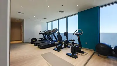 a gym with several tread machines in a room with windows at AirDXB - Chic Studio Apartment in Meydan Sleeps 2 with Balcony in Dubai