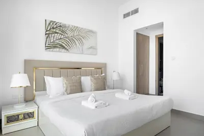 a white bedroom with a large white bed with two towels at VayK - Large 1BR Near Hospital and Mall in Dubai