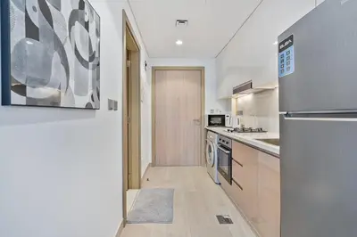 a kitchen with white walls and wooden cabinets and a refrigerator at Studio Apartment near Al Quoz Pond Park in Dubai