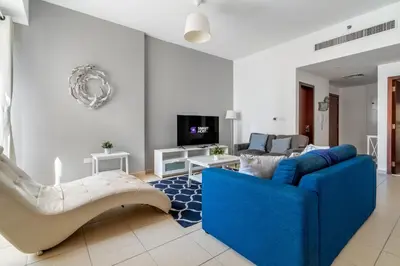 a living room with a blue couch and a tv at Spacious 2BR Flat with Gym & Pool in JBR in Dubai