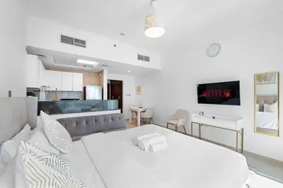 a bedroom with a large white bed and a kitchen at Spacious Studio - 10 min drive to Burj Khalifa in Dubai
