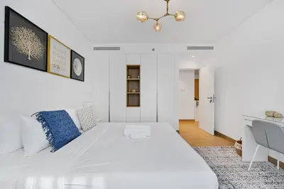 a white bedroom with a large white bed with blue pillows at Stylish 1BR Port De La Mer Escape with Beach Access in Dubai