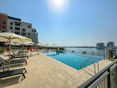 a swimming pool with chairs and umbrellas next to the water at Stylish 1BR Port De La Mer Escape with Beach Access in Dubai