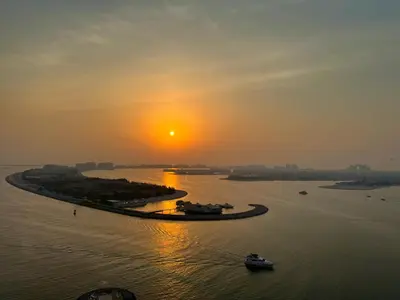 an island in the water with a sunset in the background at Luxury 2BR in Beach Vista With Stunning Palm Views in Dubai