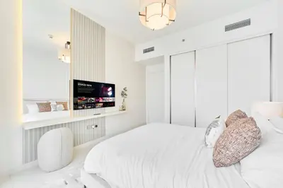 a white bedroom with a bed and a flat screen tv at Luxury 2BR in Beach Vista With Stunning Palm Views in Dubai