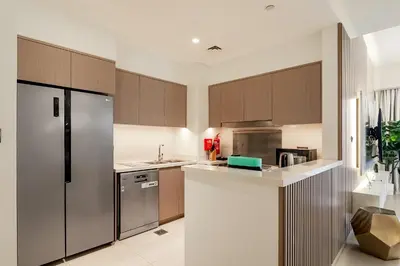 a kitchen with wooden cabinets and a stainless steel refrigerator at Burj View Stylish 3BR with Maids Room in Act One Tower Downtown in Dubai