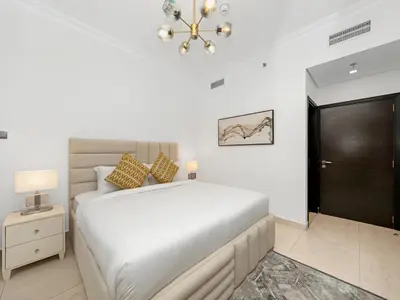 a white bedroom with a large bed and a chandelier at 5 Min to Dubai Mall Lux Stay Tennis Court in Dubai