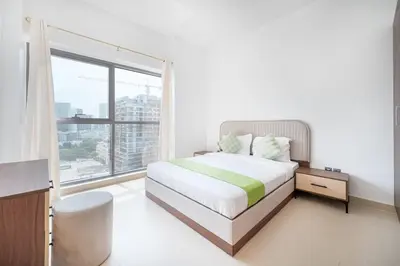 a white bedroom with a bed and a large window at Contemporary 1BHK with Home Feel in Dubai