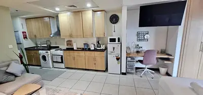 a kitchen with wooden cabinets and a white refrigerator at Higuests - Close to METRO Charming Studio with Lake Views in Dubai