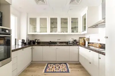 a white kitchen with white cabinets and a rug on the floor at Dubai 2BR Pool View, Near Burj Khalifa, Canal & Attractions in Dubai