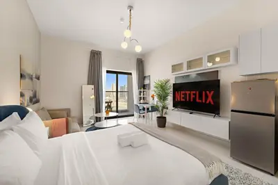 a white bedroom with a bed and a tv at Luxury Studio with Gym, Pool & Badminton Court in Dubai