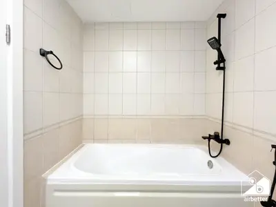 a white bath tub in a white tiled bathroom at Urban Duplex Hideaway l Gym, Pool & Balcony in Dubai