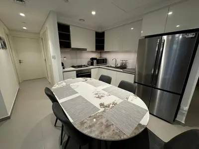 a kitchen with a table and a stainless steel refrigerator at 2min Walk to Dubai Mall - 2BR - Infinity Pool & Gym - Burj Khalifa in Dubai