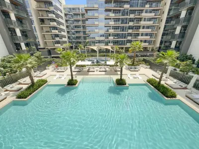 a large swimming pool with palm trees and buildings at 1BR Luxury Stay in Sobha Hartland in Dubai