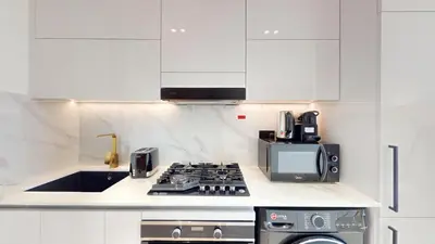 a white kitchen with a stove and a microwave at Binghatti Tulip - High Rise Upgraded Studio in JVC in Dubai