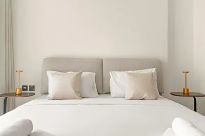 a white bed with white pillows and two tables at Vayk - Modern 1BR Apartment in JVC in Dubai