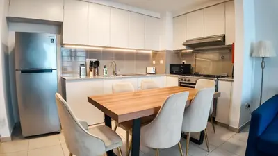 a kitchen with a wooden table and white chairs at Silk Valley - Modern 2BR Near Park & Attractions in Dubai