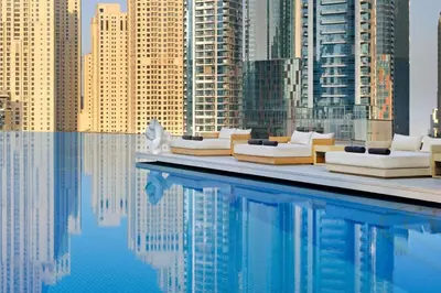 a pool with white couches and a view of a city at Waterfront Luxury 2 Bed in Marina Mall Hotel in Dubai