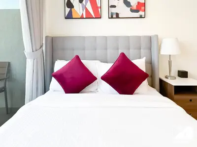 a white bed with two pink pillows on it at Amazing Studio in Meydan l Pool , Gym & Balcony in Dubai